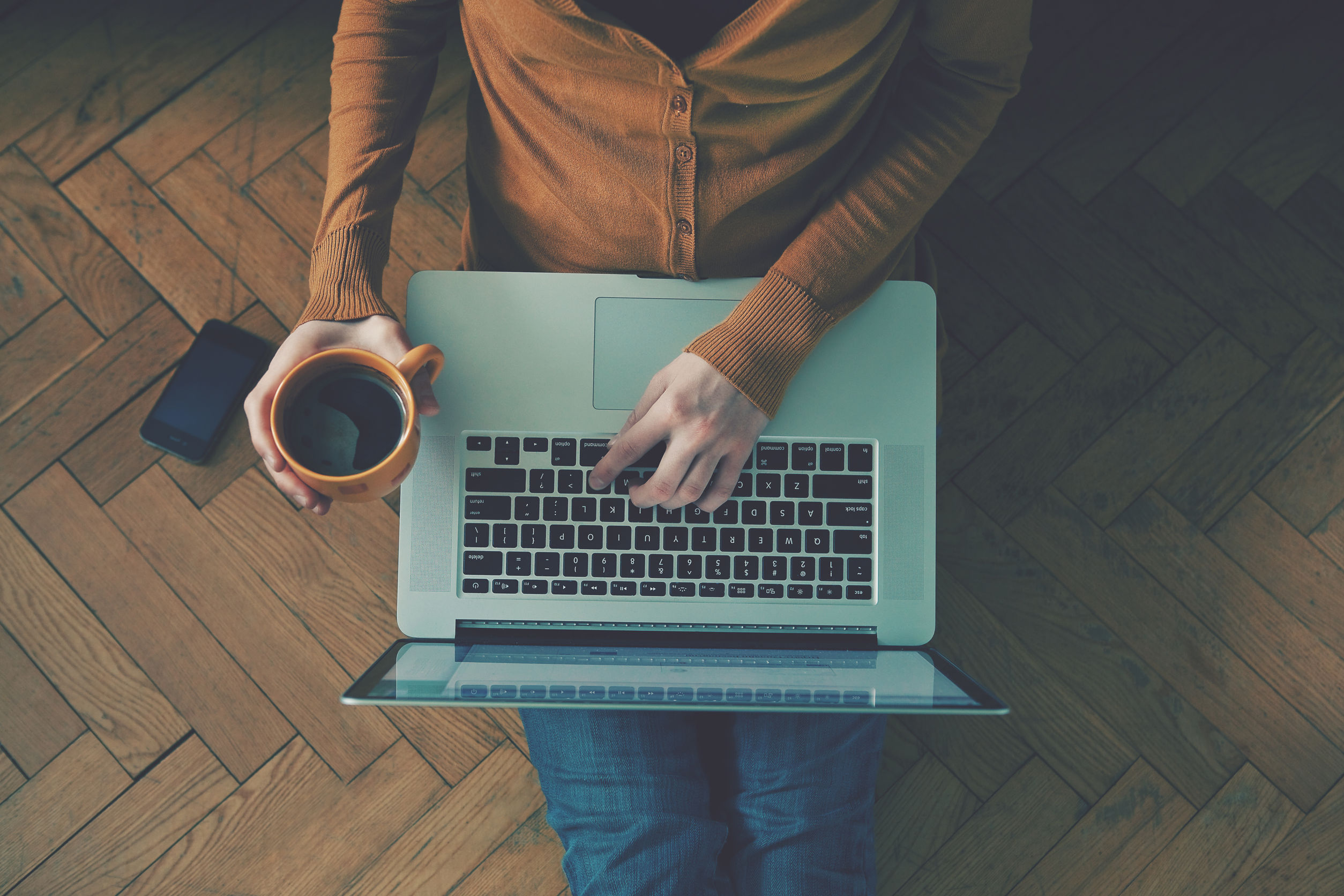 46577400 - laptop and coffee cup in girls hands sitting on a wooden floor